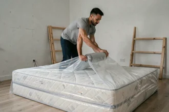 Homme emballant un matelas avec du film étirable plastique lors d'un déménagement dans une chambre à coucher