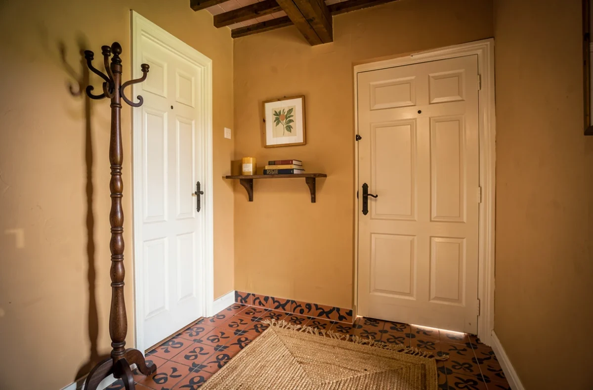 Entrée de maison de campagne avec carreaux de ciment, portemanteau vintage en bois et décoration rustique chaleureuse